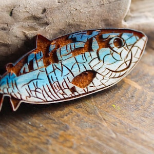 May include: A wooden fish ornament with a blue and white mosaic design. The fish has a brown wooden body and a blue and white mosaic pattern on its scales. The fish is a decorative item that can be used to add a nautical touch to any home.