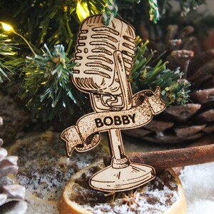 May include: A wooden Christmas ornament shaped like a vintage microphone with a banner that reads "BOBBY".