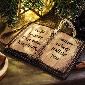May include: Wooden Christmas ornament shaped like an open book, with the text "I will honour Christmas in my heart, and try to keep it all the year." The ornament is surrounded by festive decorations, including cinnamon sticks and greenery.
