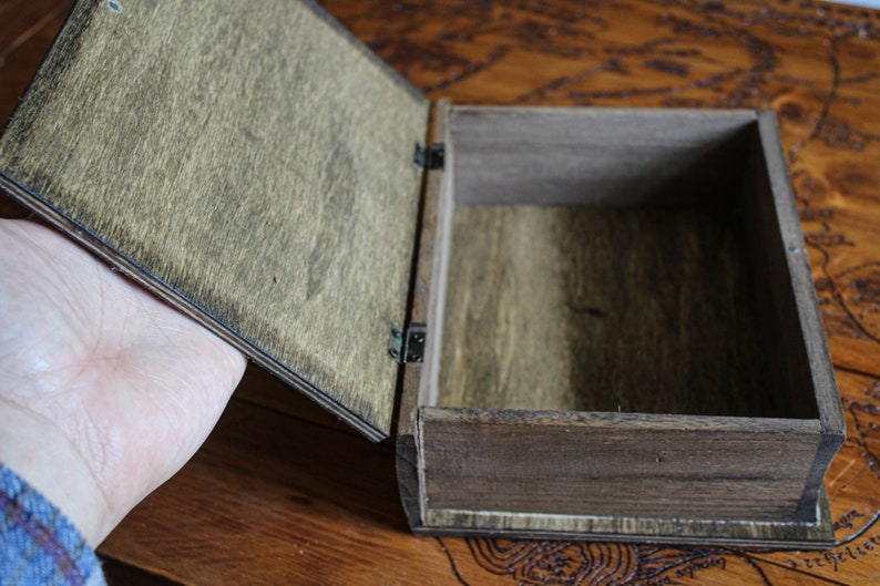 May include: A wooden box with a hinged lid, open to reveal the empty interior. The box is made of dark brown wood with a natural wood grain.