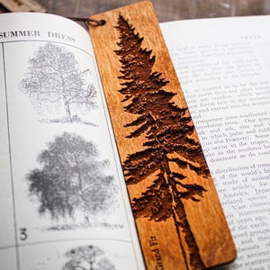 May include: A wooden bookmark featuring a laser-engraved image of a Grand Fir tree. The bookmark is brown and has a natural wood grain.