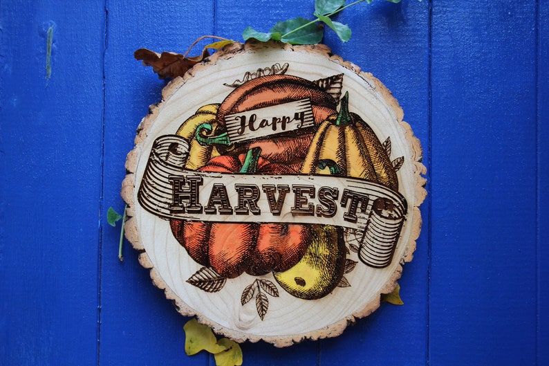May include: A wooden round sign with a brown, orange, and yellow illustration of pumpkins and the text "Happy Harvest".