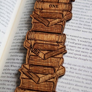 May include: A wooden bookmark shaped like a stack of books. The bookmark is engraved with the words "Just One More" and "Chapter".