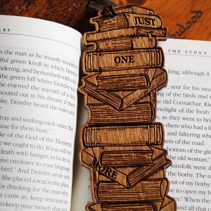 May include: A wooden bookmark with a stack of books engraved on it. The bookmark is brown and has the words "Just One More" engraved on it.