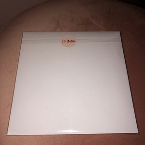 May include: A white, rectangular piece of paper with a round, white sticker in the upper right corner. The sticker has red text that reads "LC Bella".