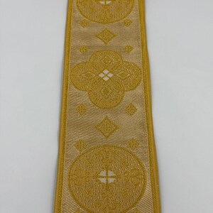 May include: Gold-colored ribbon with repeating circular and diamond patterns. The ribbon has a textured appearance and is bordered by a lighter gold trim. The text "EMMA 253 No.2" is printed on the ribbon.
