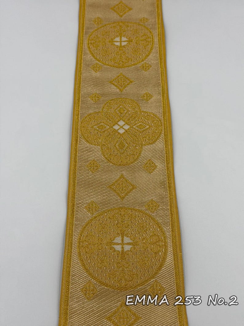 May include: Gold-colored ribbon with repeating circular and diamond patterns. The ribbon has a textured appearance and is bordered by a lighter gold trim. The text "EMMA 253 No.2" is printed on the ribbon.