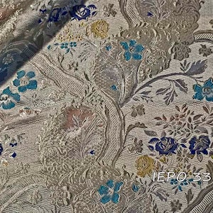 Pode incluir: Close-up de um tecido prateado com um padrão floral. O tecido tem uma textura em relevo e apresenta flores azuis, amarelas e rosas. O texto "IEPO 33 101" é visível no canto inferior direito.