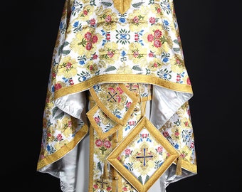 May include: White liturgical vestment with gold and floral embroidery. The vestment has a long, flowing robe with a decorative collar and a sash. The fabric is richly decorated with intricate patterns and designs.
