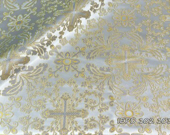 May include: White fabric with a gold brocade pattern of crosses and floral designs. The fabric has a subtle sheen and a luxurious feel. The text "IEPO 102 103" is printed in the bottom right corner.