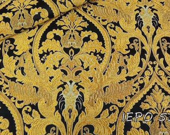 May include: Black fabric with a gold damask pattern. The fabric has a raised texture and a luxurious feel. The fabric is perfect for upholstery, curtains, or other home decor projects.