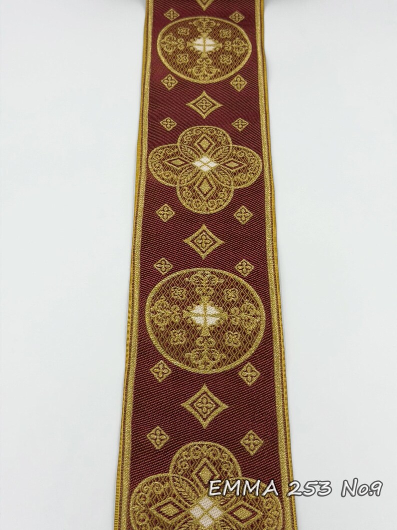 May include: Burgundy ribbon with gold embroidered floral and geometric patterns. The ribbon features repeating circular and diamond shapes, with the text "EMMA 253 No.9" at the bottom. The edges are trimmed with gold.