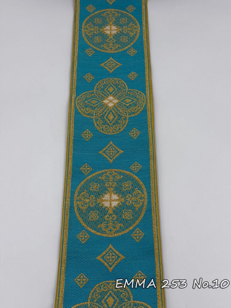 May include: A teal ribbon with gold floral patterns and borders. The ribbon features repeating circular, diamond, and quatrefoil designs. The text "EMMA 253 No.10" is printed in gold at the bottom of the ribbon.