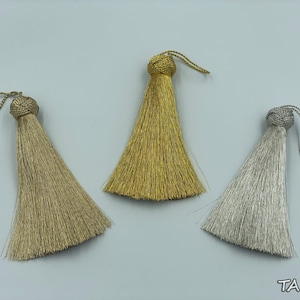 May include: Three tassel ornaments in gold, silver, and bronze colours. The tassels are made of a soft, shiny material and have a loop at the top for hanging.