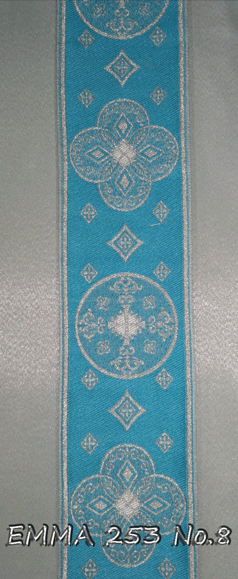 May include: A turquoise ribbon with a silver geometric pattern. The ribbon features repeating floral and diamond shapes. The text "EMMA 253 No.8" is printed at the bottom. The ribbon is bordered with a silver trim.