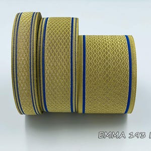 Puede incluir: Tres rollos de cinta de rayas doradas y azules. La cinta tiene un patrón texturizado y está ribeteada con una fina línea azul. La cinta está etiquetada como "EMMA 193 No.04".
