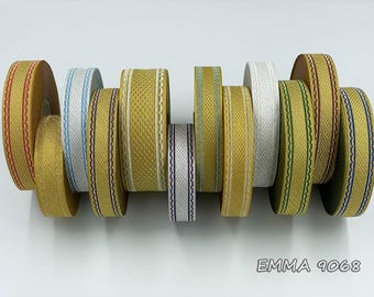 Puede incluir: Una colección de carretes de cinta decorativa en varios colores, incluyendo dorado, blanco y azul. Las cintas presentan diseños tejidos y estampados, algunos con bordes festoneados. El texto "EMMA 9068" es visible en la parte inferior.