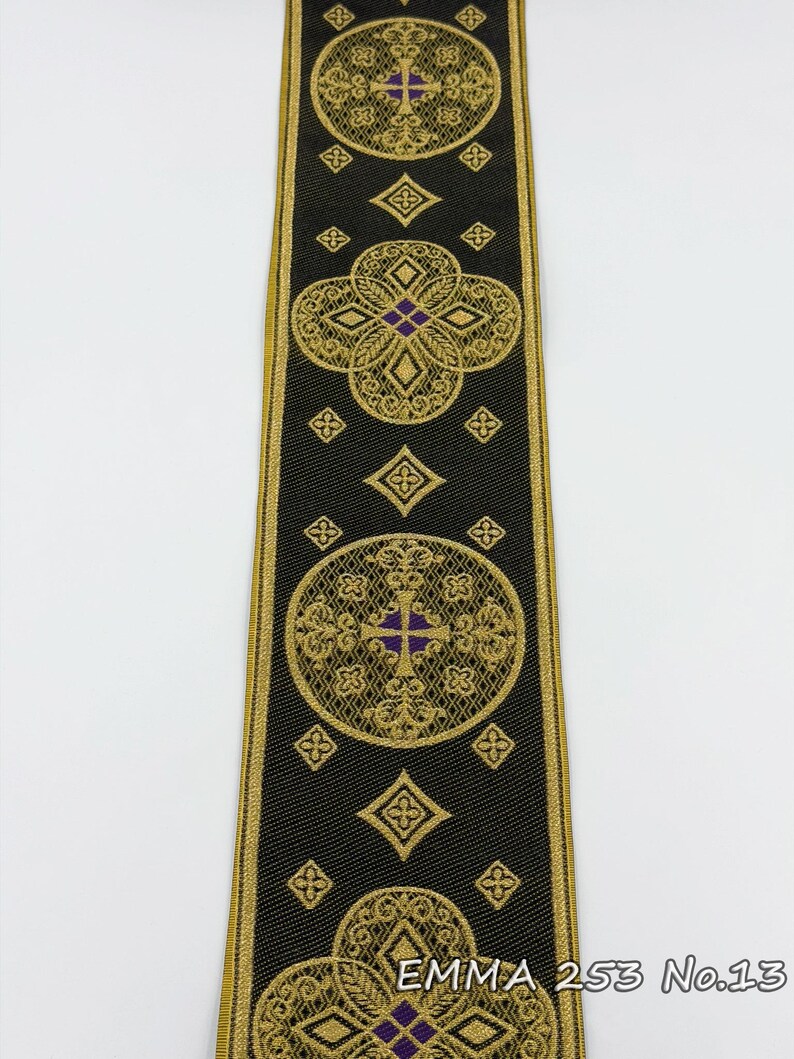 May include: Black ribbon with gold and purple embroidered geometric designs. The ribbon features repeating circular and diamond patterns with a cross motif. The text "EMMA 253 No.13" is visible on the ribbon.