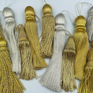 Könnte beinhalten: Eine Sammlung von 10 dekorativen Quasten in Gold- und Silberfarben. Die Quasten sind aus einem weichen, seidenartigen Material gefertigt und haben verschiedene Formen und Größen.