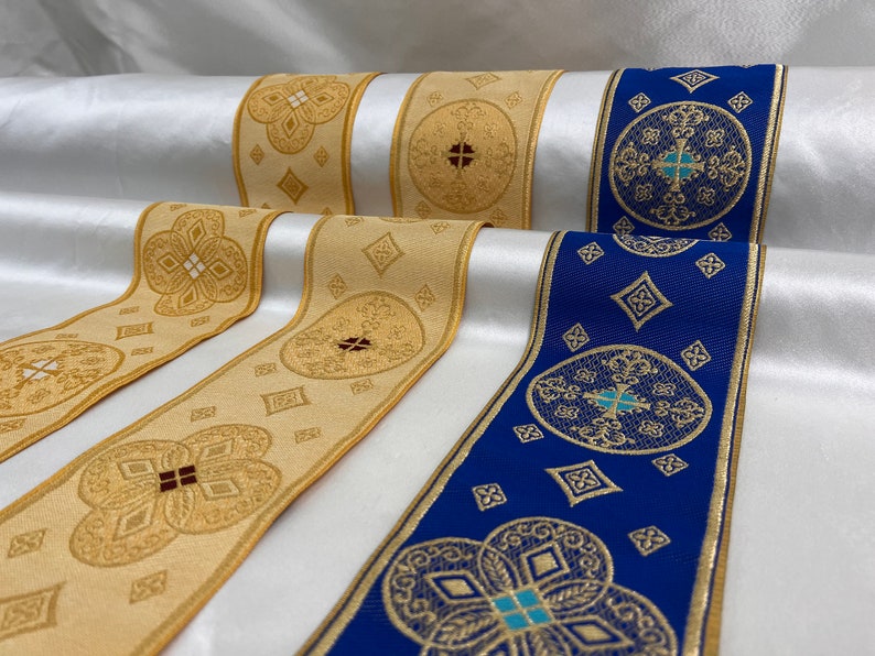 May include: Close-up of decorative ribbon rolls. The ribbons feature intricate gold patterns on a cream and blue background. The designs include crosses, diamonds, and floral motifs, suitable for religious or ceremonial use.