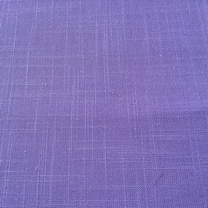 May include: Close-up of a textured, solid purple fabric. The weave of the material is visible, creating a grid-like pattern. The color is a vibrant, medium purple, with subtle variations in tone across the surface. The fabric appears to be a linen or similar material.