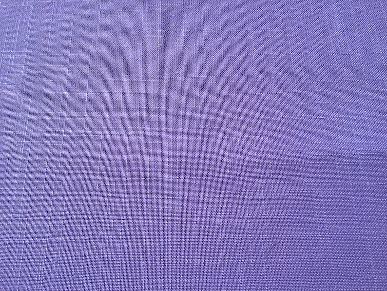 May include: Close-up of a textured, solid purple fabric. The weave of the material is visible, creating a grid-like pattern. The color is a vibrant, medium purple, with subtle variations in tone across the surface. The fabric appears to be a linen or similar material.