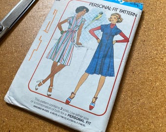 Może przedstawiać: Wzór szycia Simplicity w stylu vintage z ilustracjami dwóch kobiet w sukienkach. Wzór jest oznaczony jako "PERSONAL FIT PATTERN" i zawiera informacje o rozmiarach. Nożyczki i szpulki nici są widoczne w tle.