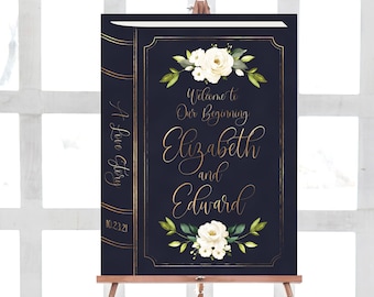 May include: A navy blue wedding sign with gold accents and white flowers. The sign reads "Welcome to Our Beginning Elizabeth and Edward 10.23.21" and "A Love Story".