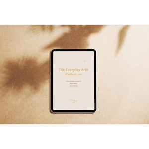 Puede incluir: Una tableta digital que muestra el texto "The Everyday AHA Collection" en color beige claro. La tableta está sobre un fondo neutro con sombras, creando una estética minimalista. También se ve el texto "Tiny human moments. Real clarity. Zero drama."