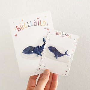 Può includere: Due toppe da stirare con una balena blu con stelle bianche. La toppa più grande dice "Bügelbild" e la toppa più piccola dice "Bügelbild Mini".