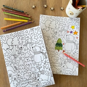 Puede incluir: Dos páginas para colorear en blanco y negro con un tema navideño de invierno con osos polares, estrellas, árboles y otros elementos festivos. Las páginas están sobre una superficie de madera con lápices de colores.