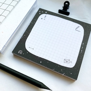 Może przedstawiać: Czarno-biały notes w kratkę z czarną ramką i białymi gwiazdkami, księżycami i innymi ilustracjami. Notes ma zaokrąglony róg, a w prawym górnym rogu widnieje napis "To-do".