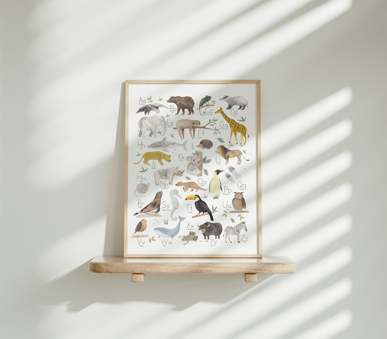 May include: A framed alphabet poster with illustrations of animals for each letter. The animals are drawn in a whimsical style with watercolor and include a sloth, a giraffe, a penguin, a toucan, and a zebra.