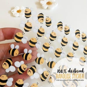 Könnte beinhalten: Bogen mit transparenten Aufklebern mit Cartoon-Bienen mit gelb-schwarz gestreiften Körpern und weißen Flügeln. Die Aufkleber haben lächelnde Gesichter und sind für die Verwendung auf glatten Oberflächen konzipiert. Der Text "100% deckend RANDLOSE STICKER" ist sichtbar.