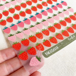 Peut inclure: Feuille d'autocollants fraises rouges et roses avec des feuilles vertes. Les autocollants sont disposés en rangées sur un support transparent. Le texte "BÜGELBILDER" est visible en bas à droite.