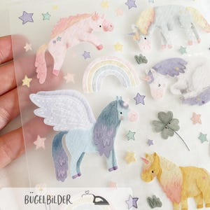 May include: A sheet of colorful unicorn and star stickers in pastel colors. The stickers include unicorns in pink, blue, and yellow, a rainbow, and various stars. The text "BÜGELBILDER" is at the bottom.