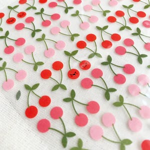 Op de afbeelding: Een vel met kersenstickers in rood- en roze tinten, met groene stelen en bladeren. Sommige kersen hebben lachende gezichten. De stickers zijn gerangschikt in een herhalend patroon, geschikt voor knutselen of decoratie.