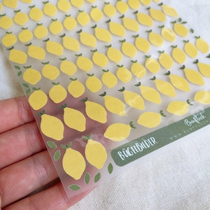 Può includere: Foglio di adesivi di limoni gialli con foglie verdi. Gli adesivi sono su un supporto trasparente. Il testo "BÜGELBILDER" è stampato su un'etichetta verde.