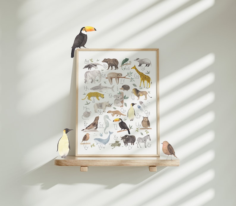 May include: A colorful alphabet poster featuring animals from around the world. Each letter is paired with an animal illustration, such as a toucan for "T" and a zebra for "Z". The poster is framed in wood and displayed on a shelf with a penguin and a bird figurine.