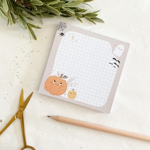 May include: A set of Halloween themed sticky notes with a grid pattern. The notes feature a pumpkin, a ghost, bats, and a spider web.