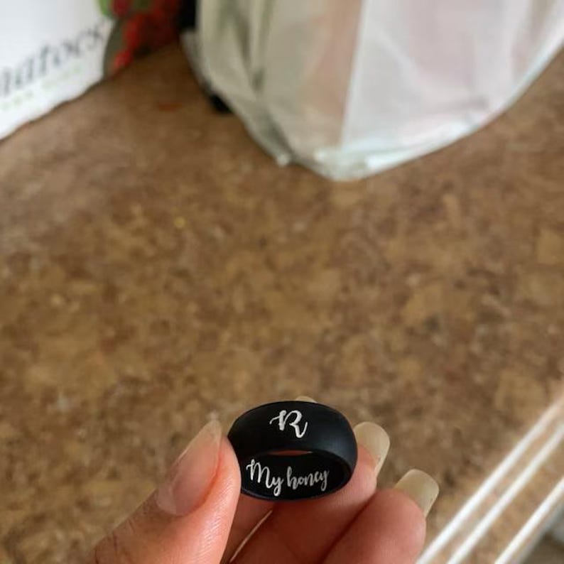 May include: A black silicone ring engraved with the letter "R" and the words "My honey" in white.