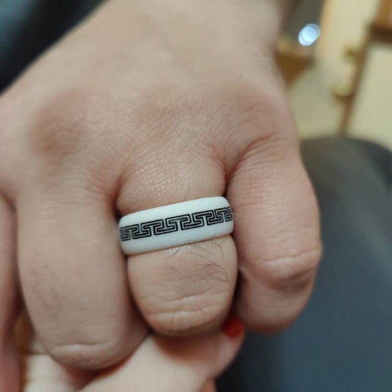 May include: A white silicone ring with a black geometric pattern. The ring is worn on a person's finger.