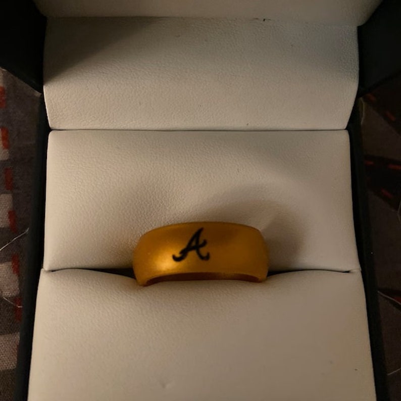 May include: A gold silicone ring with a black "A" engraved on the top.