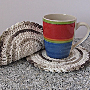 May include: A ceramic mug with horizontal bands of red, orange, green, and blue, resting on a circular, cream, tan, and brown crocheted coaster, with a second identical folded coaster positioned vertically behind the mug.