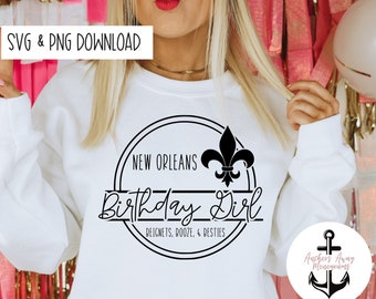 Pode incluir: Uma camisa de moletom branca com um design circular preto que diz "New Orleans Birthday Girl" com uma flor-de-lis e o texto "Beignets, Booze, & Besties".