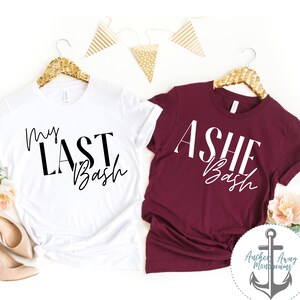 May include: Two white t-shirts with black text. One shirt says "My Last Bash" and the other says "Ashe Bash".