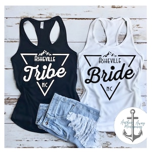 May include: Two black and white tank tops with a triangle design featuring the text "Asheville Tribe NC" and "Asheville Bride NC".