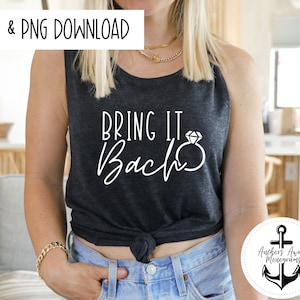May include: A gray tank top with the text "Bring It Back" in white script with a diamond ring graphic. The tank top is tied at the waist and the model is wearing blue jeans.