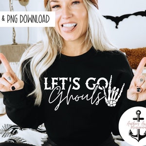 May include: Black sweatshirt with the text "Let's Go Ghouls" in white lettering. The text is accompanied by a white skeleton hand making the "rock on" hand gesture.