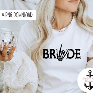 May include: White t-shirt with the word "BRIDE" in black letters. The "I" in bride is replaced with a skeleton hand making the "I love you" hand gesture.